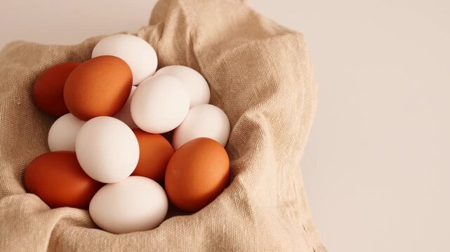 A collection of white and brown eggs placed together in a cloth bowl full of eggs.
