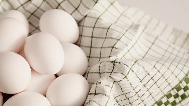 Fresh white eggs are arranged neatly in a kitchen cloth on a clean white surface for cooking.