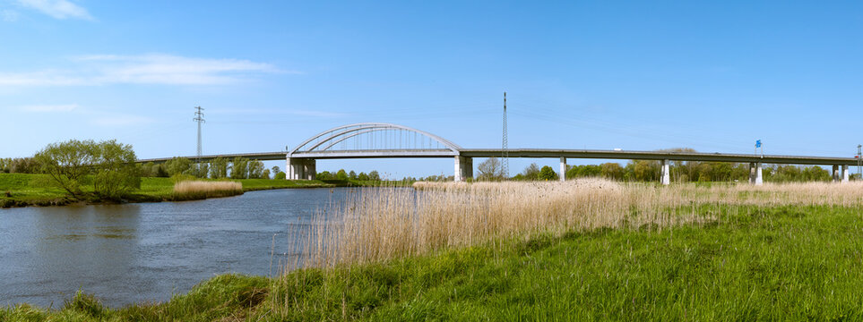 Modern highway arch bridge spanning the St&ouml;r River near Itzehoe, Schleswig-Holstein, Germany, under bright blue sky.