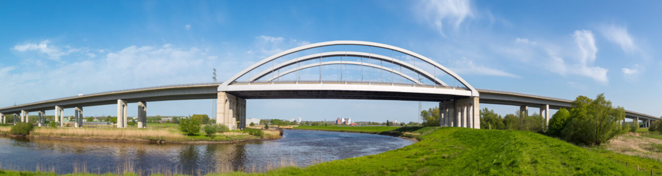Modern highway arch bridge spanning the St&ouml;r River near Itzehoe, Schleswig-Holstein, Germany, under bright blue sky.