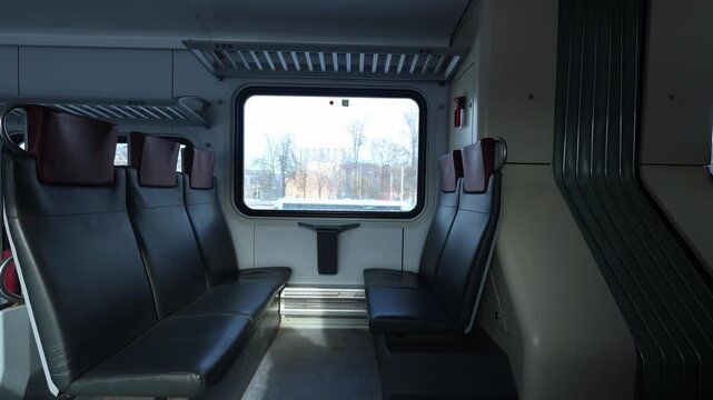 An empty train compartment with black seats and a window showing a passing urban landscape.