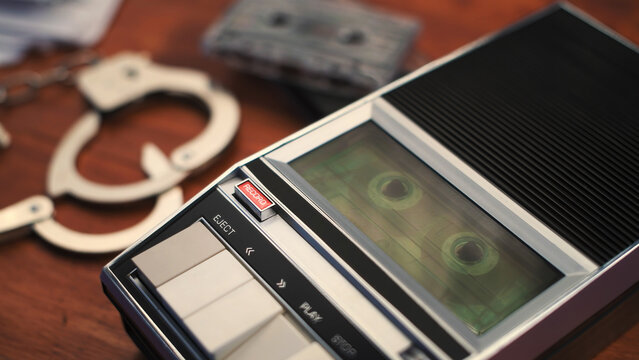 Handcuffs and vintage cassette recorder on wooden table, crime concept