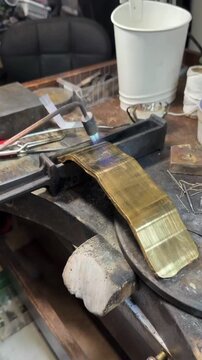 Craftsman applying gold leaf gilding to wooden surface with wide brush and tools on workshop bench close up traditional restoration technique for luxury decor sign making and antique repair