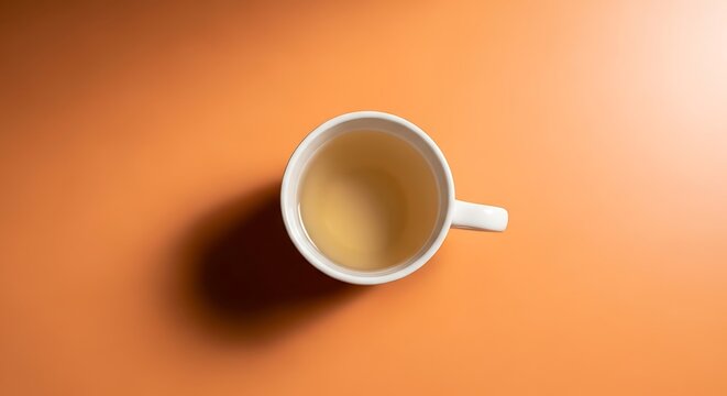 Overhead view of a white mug filled with pale liquid on an orange gradient background