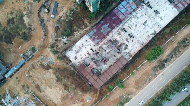 Aerial drone shot looking down moving forward over construction site with crane, roof installation, cement mixing plant and equipment showing the mess and chaos of a real estate development
