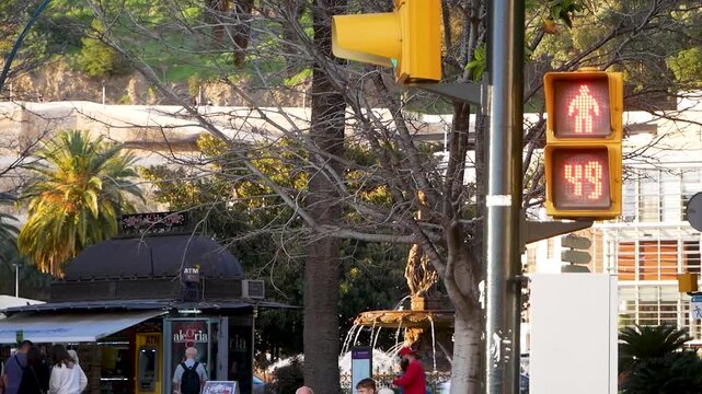 Pedestrian red traffic signal with digital countdown timer in Malaga city, Spain. Mediterranean urban street with palm trees, fountain and people in Andalusia. European travel and transportation conce