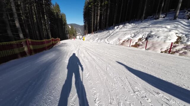 Shadow of a skier rides down a ski slope First person fast motion of skier skiing on slope after in ski resort, enjoying beautiful landscape of mountains covered with snow in sunny winter day. Concept