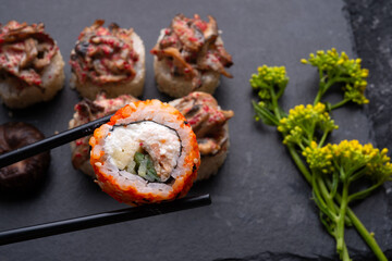 sushi roll in chopsticks and  shiitake mushrooms  beautiful served  at black dish. top view. macro shot