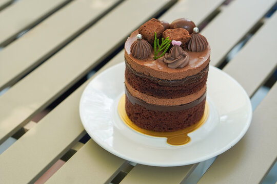 Closeup brown chocolate cake with layers of chocolate pudding and coffee pudding layers, decorated with chocolate ball, silver sprinkle and green grass, on a golden paper, are put on a white ceramic  
