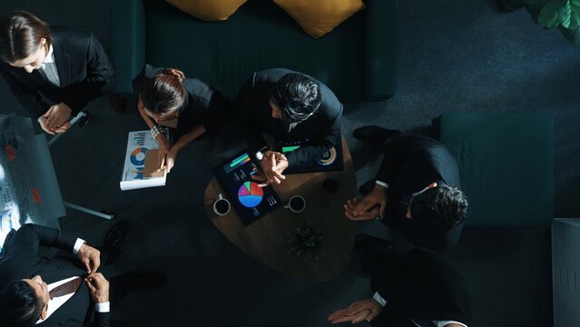 Top down view of business team listen investor present idea while standing at whiteboard. Diverse group sitting while placed tablet displayed financial graph or investment statistic. Directorate.