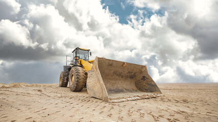 A bulldozer or loader moves across sandy terrain with a large dump ahead. Earthworks are being prepared for a construction project