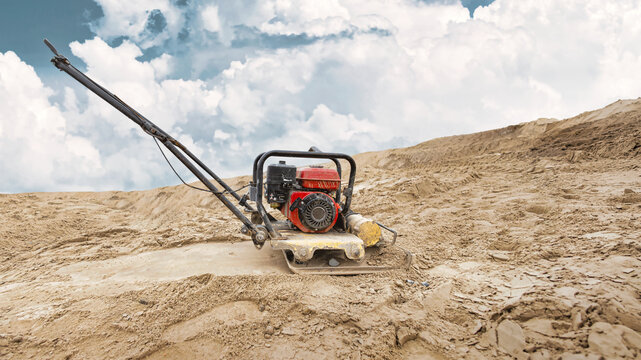 A vibratory plate compactor works on a sandy area at a construction site. Preparing the foundation for construction