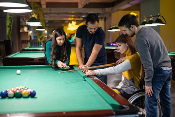 Fototapeta premium Young woman who uses a wheelchair playing billiards with friends