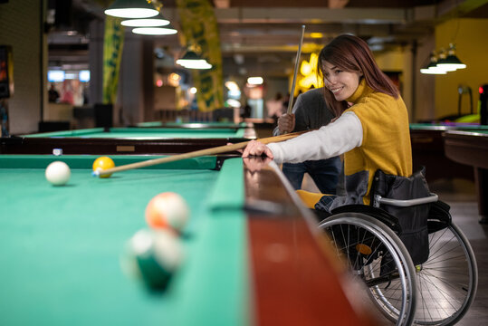 Young woman who uses a wheelchair and who is paralyzed playing billiards