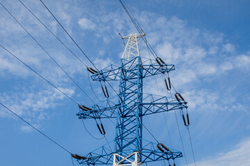 a tall metal power transmission line support against a blue sky with white clouds