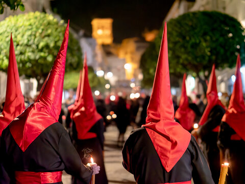 Many nazarenos with red hoods walking in procession