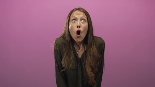 Woman gasping with open mouth in pink studio set, frontal pose wearing olive shirt and necklace, wide open expression; sudden surprise.