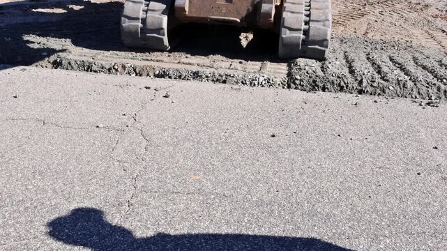 Heavy tractor machinery spreads gravel on road surface while workers oversee process in broad