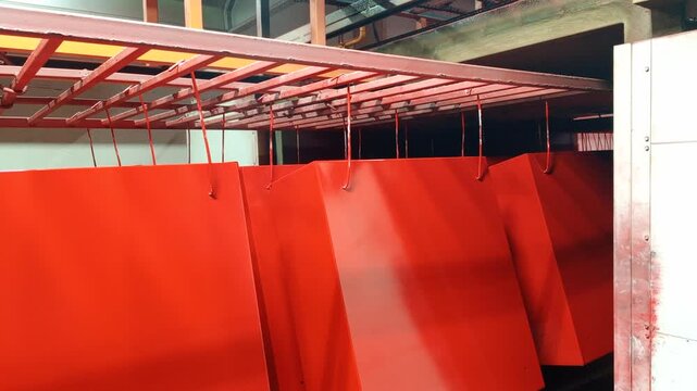 Powder coated metal cabinets exit the curing oven and are transported outside by an automated walking beam conveyor system in industrial manufacturing facility.