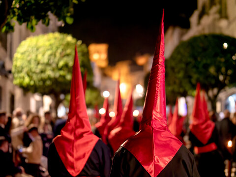 Many nazarenos with red hoods walking in procession