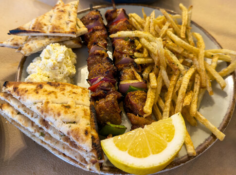 Greek souvlaki skewers served with crispy fries, pita bread and lemon on a taverna table in Greece. Closeup above view