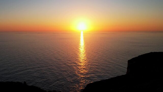 Aerial drone view of the Highest point of Malta at Dingli Cliffs, beautiful lush green grass and rock formations with a steep drop to the sea at sunset, golden hour. Sun giving the golden glow