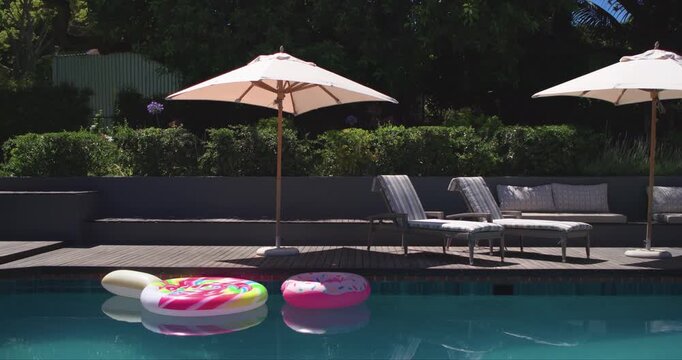 Two inflatable rings are drifting leftward near pool edge as light breeze is pushing them