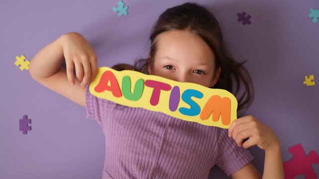 An autistic girl shows a card with the word autism. The diversity of people on the autism spectrum.
