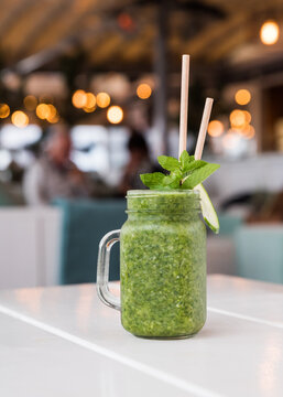 A healthy green smoothie in a juice glass with mint leaves and straws on a white table in a caf&eacute; restaurant.