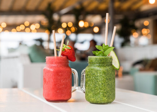 Healthy fresh red and green smoothies in a juice glasses with straws on a white table in a caf&eacute; restaurant.