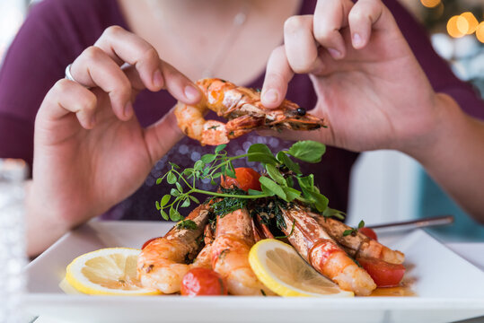 Someone picking up grilled fresh cooked shrimp prawns off a plate in a restaurant