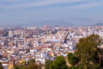 Obraz premium Malaga Spain vast high angle vista of the dense urban residential districts and rooftops stretching toward the misty mountain peaks of the Sierra de Mijas range in the distance.