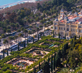 Fototapeta premium Malaga Spain wide panoramic high angle view showing the Malaga City Hall facade and the symmetrical Pedro Luis Alonso Gardens with palm trees and walking paths in the city center.