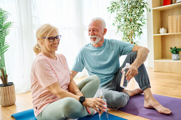Obraz premium Portrait of a senior couple holding water bottle and exercise mat smiling and talking at home healthy living
