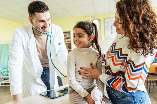 A mother brings her daughter to the doctor for a checkup, staying close to comfort her. The moment feels caring and protective, focused on the child&rsquo;s health and reassurance.