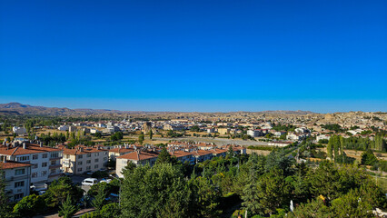 Obraz premium Suburban Town Under Clear Blue Sky, Tree Canopy And Mixed Rooftops, Grid Of Streets, Parks And Residential Blocks Stretching Toward Distant Hills.