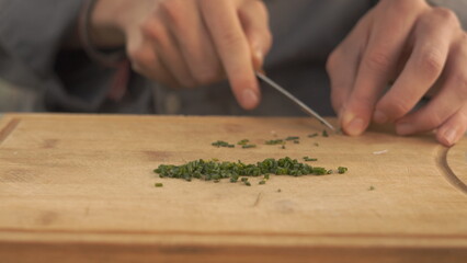 Obraz premium Chopping fresh chives on wooden cutting board – close up food preparation in kitchen