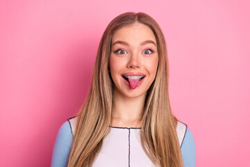 A young girl playfully sticks her tongue out with confidence against a bright pink background © deagreez