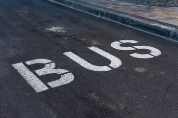 Bold White Letters on Asphalt Announce the Designated Space for Bus Parking in a Quiet Urban Setting Under the Warm Sunlight of a Late Afternoon
