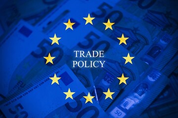Stock image illustrating EU trade policy and carbon tax. Euro banknotes overlay the European Union flag, representing the financial impact of CO2 emissions, carbon pricing, decarbonization, and green 