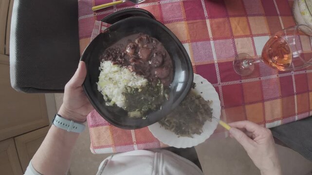 Authentic Brazilian feijoada served with white rice and saut&eacute;ed greens. Traditional South American dish photographed from above in a home dining setting.