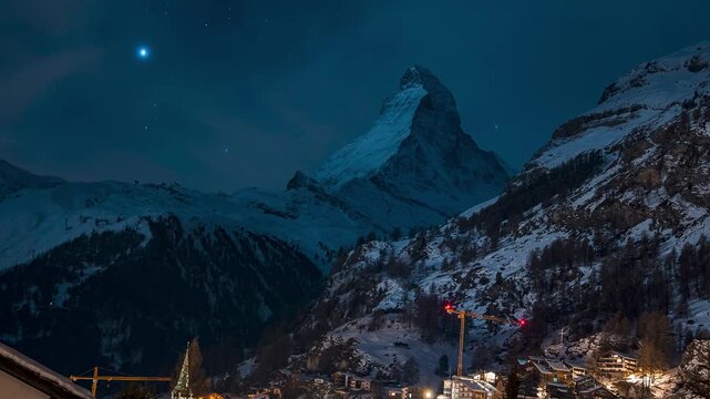 Timelapse over Zermatt in Switzerland at night. Swiss ski resort. The Matterhorn in the background during starry night with Orion constellation visible over the Matterhorn. Famous alpine village.