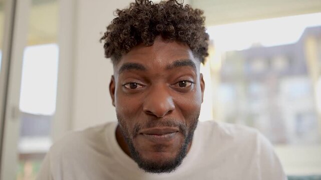 Young man smiling and speaking directly to camera indoors. Friendly, upbeat close-up capturing positive emotions, confidence, and authentic communication in a modern lifestyle or vlog setting