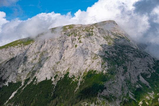 Landscape of a massive rocky mountain reflecting bright sunlight and reaching thick white clouds