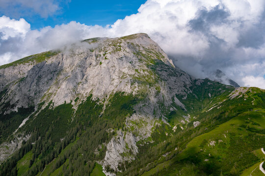 Scenic photo of a high mountain with a rocky peak and lush vegetation below on a sunny day