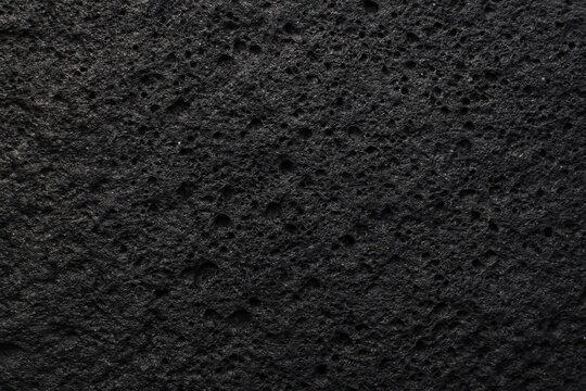 Black volcanic basalt rock surface with dense porous cavity texture