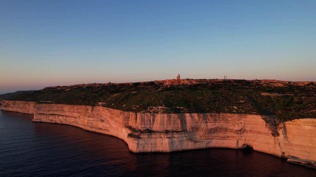 Aerial drone view of the Highest point of Malta at Dingli Cliffs, beautiful lush green grass and rock formations with a steep drop to the sea at sunset, golden hour. Sun giving the golden glow