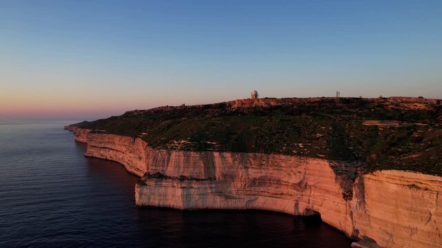 Aerial drone view of the Highest point of Malta at Dingli Cliffs, beautiful lush green grass and rock formations with a steep drop to the sea at sunset, golden hour. Sun giving the golden glow