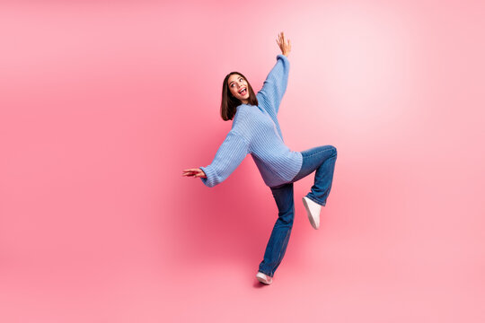 Young woman in blue knit sweater and jeans leaps with joy against pink background for a bright casual lifestyle fashion and advertising image