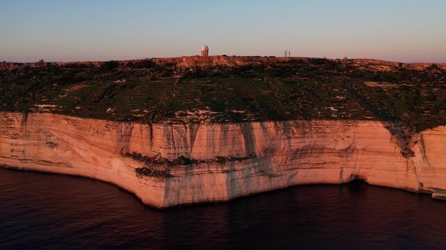 Aerial drone view of the Highest point of Malta at Dingli Cliffs, beautiful lush green grass and rock formations with a steep drop to the sea at sunset, golden hour. Sun giving the golden glow